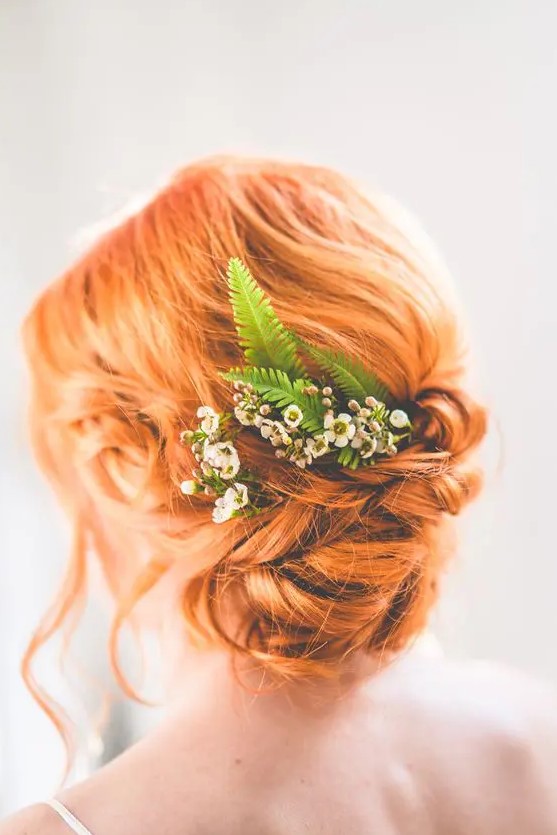 a gorgeous ginger twisted low updo with some locks down and some fresh blooms and greenery is a cool idea for a boho bride