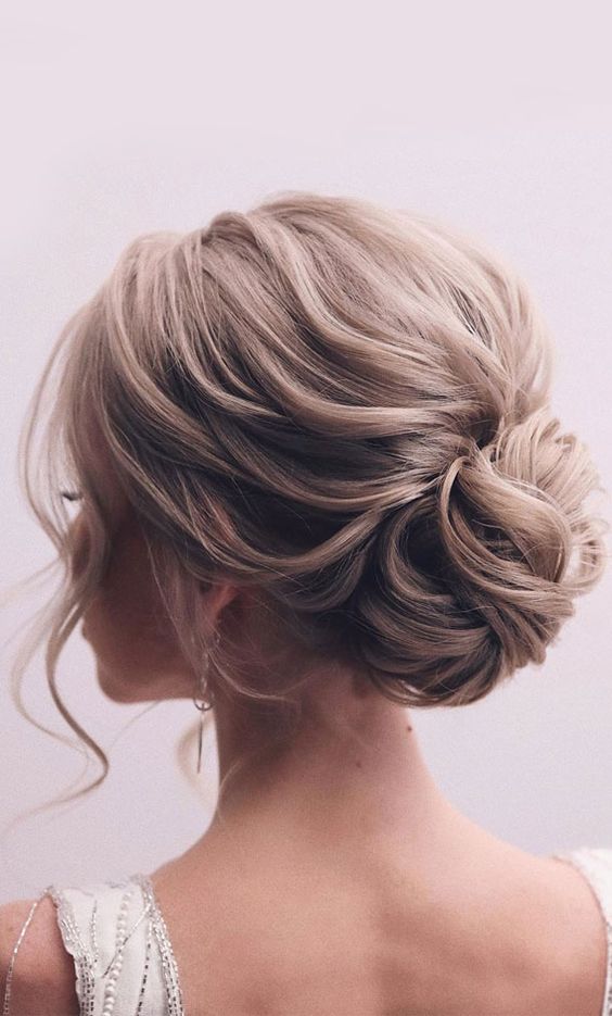 an elegant wavy wedding updo with a chignon and a wavy volume on top, with some locks down is chic