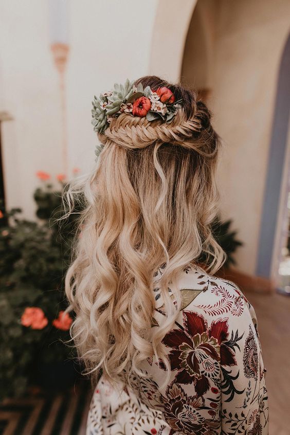 a beautiful boho wedding hairstyle with a fishtail braid halo, waves down and bold blooms and pale leaves tucked in