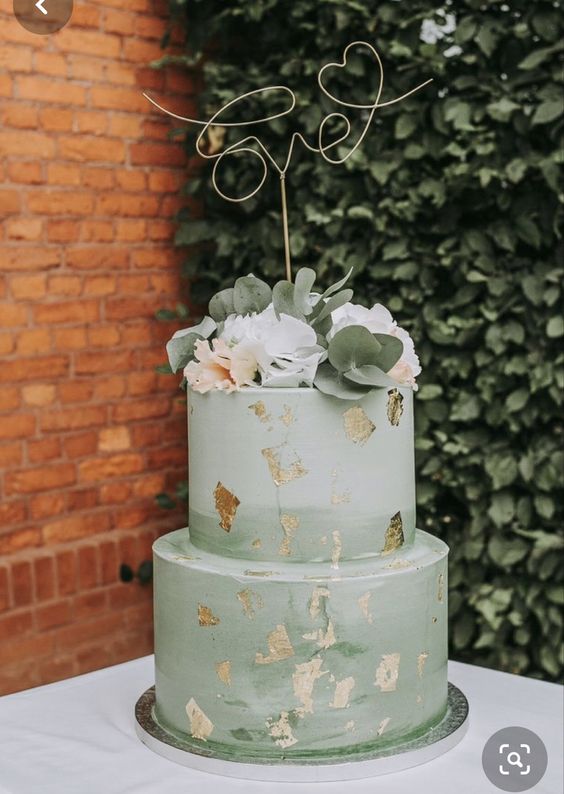 an ombre sage green wedding cake with gold leaf, neutral blooms and eucalyptus and a calligraphy topper
