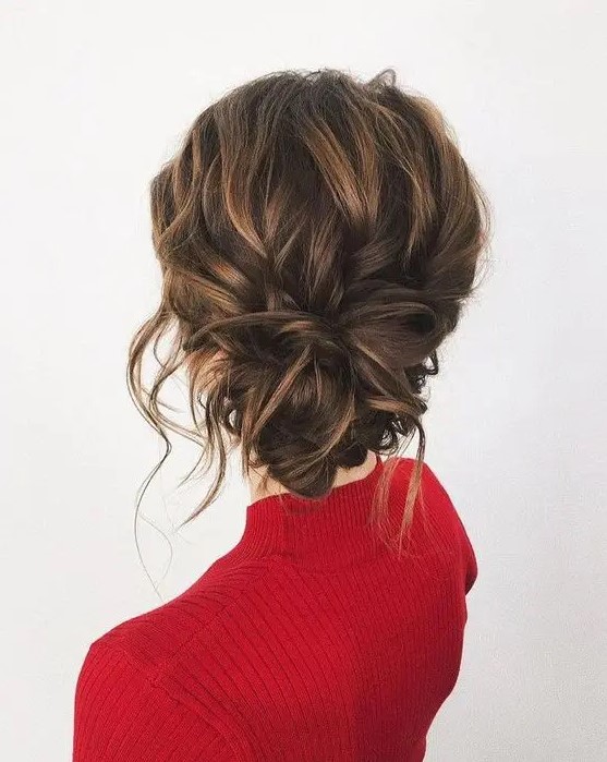 a messy wavy updo with a low twisted bun, some locks down and a volume on top