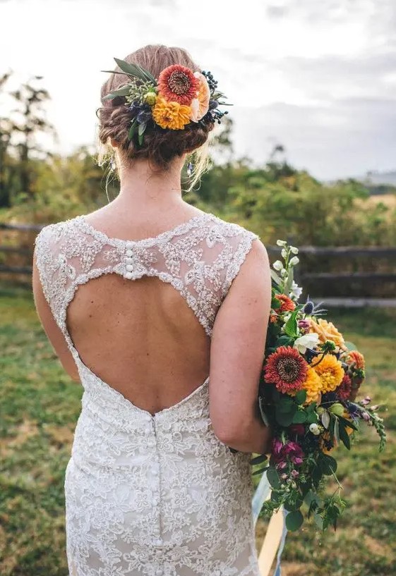 a braided low updo with a volume on top and lush bold fall flowers as an accent is cool for a rustic bride