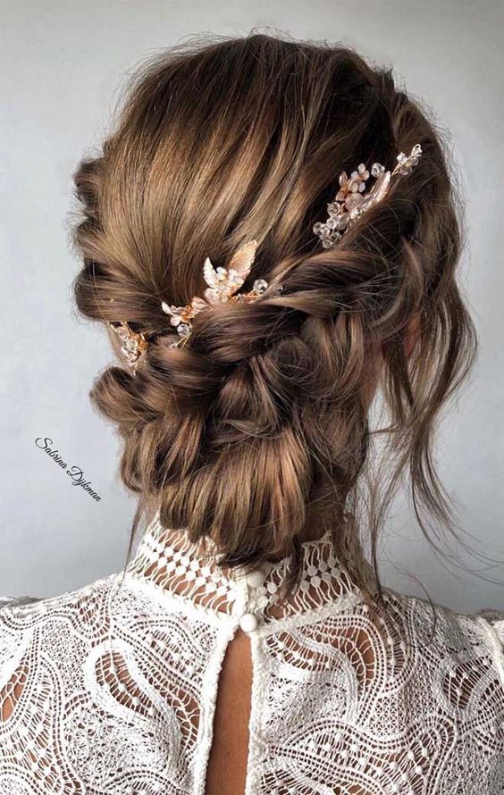 a braided low updo with two side braids, a bump, a low bun and face-framing locks plus some beaded hair pieces