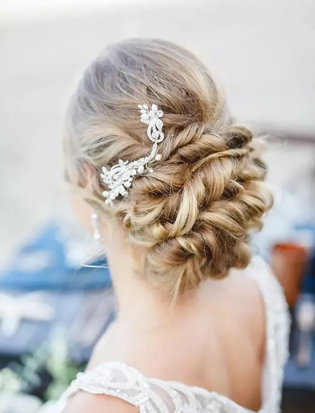 a twisted low updo on long hair with a rhinestone hairpiece on one side for a refined look at a beach or some other wedding