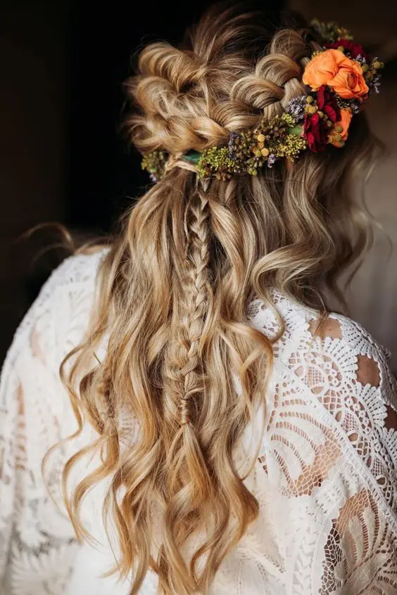 a fantastic boho wedding hairstyle with a loose braided halo, a long briad and waves down and some bright blooms