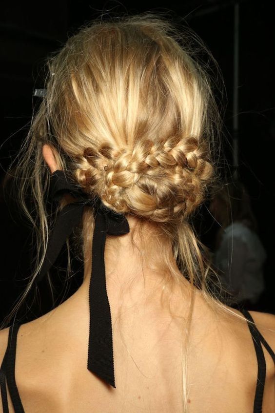 a creative braided low updo with a messy top, some hair down and a black ribbon bow is a stylish idea for a modern bride