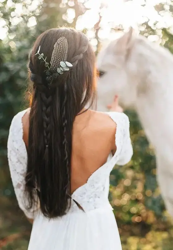 a half updo with braids hanging down adorned with a feather, berries and eucalyptus is great for a boho bride