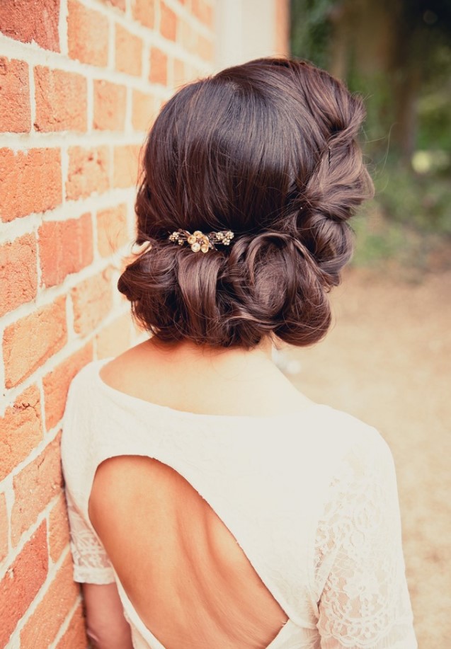 a vintage low updo with a twisted and wavy lower part and a volume on top plus a small hairpiece