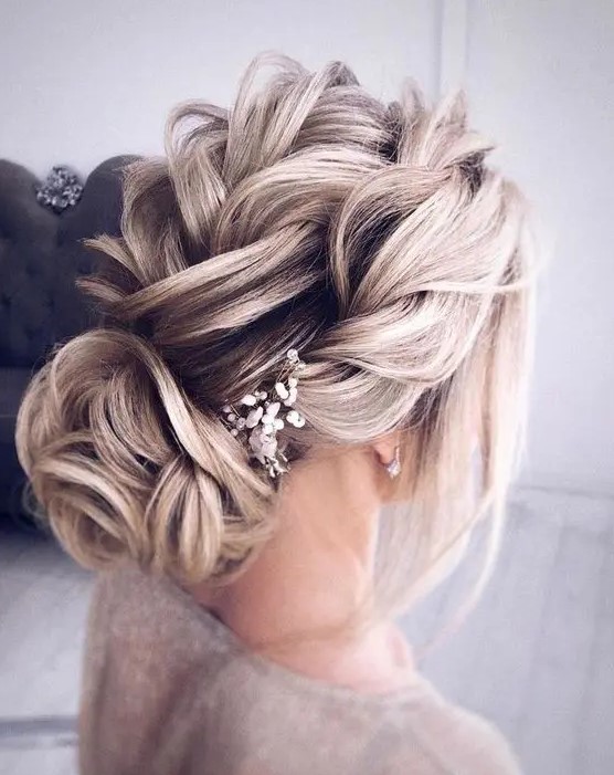 a loose textural braided updo with a twisted bun and some baby's breath tucked in is a cool idea for long hair