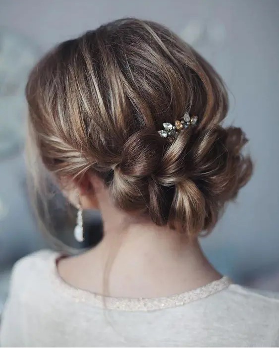 an elegant updo with a large braided element, a bump and a rhinestone hairpiece for a romantic feel