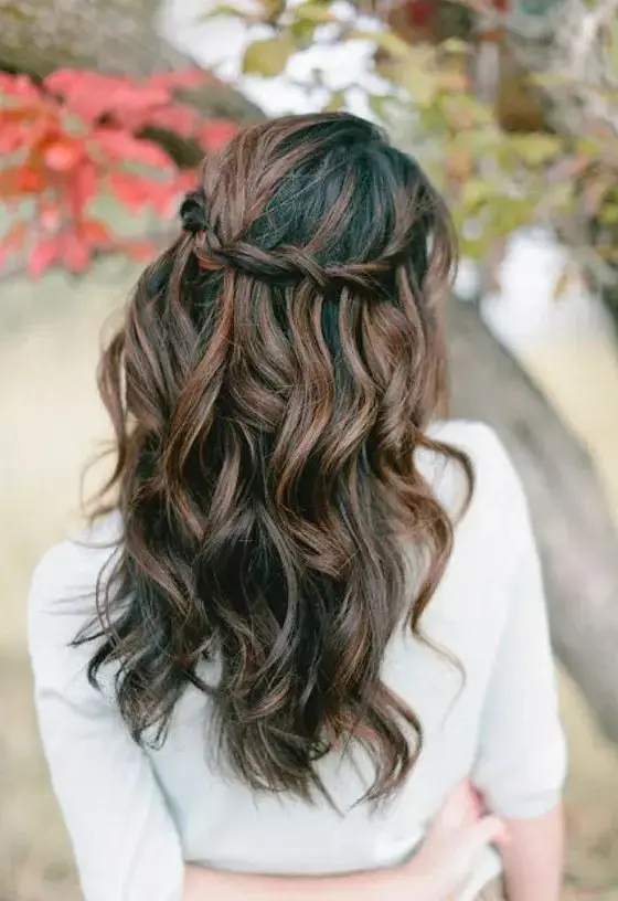 a chic twisted halo wavy half updo looks especially interesting with balayage