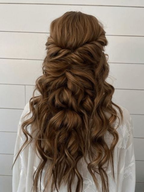 a long twisted and wavy half updo with a bump on top and waves down plus a looped halo is a cool and chic idea