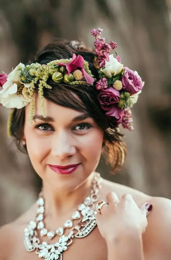 a short wavy hairstyle with a lush floral crown with fuchsia blooms, white flowers and greenery and a matching lipstick