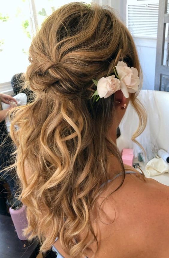 a twisted wedding half updo with a messy wavy bump and waves down plus some fresh blooms is classics