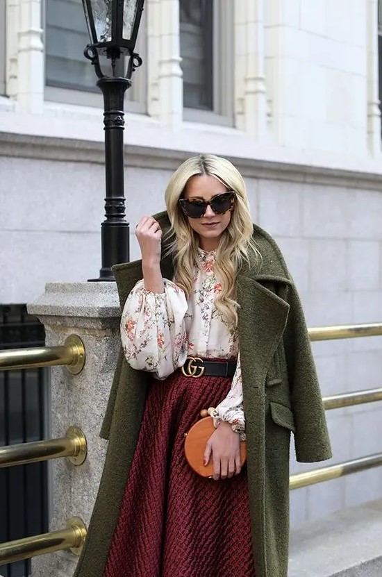 a floral blouse, a burgundy tweed A-line midi skirt, a green coat and a round orange bag for a winter wedding