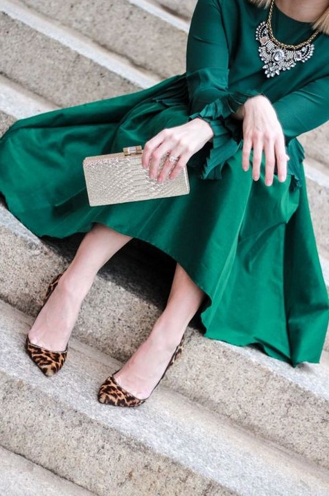 An A line emerald skirt, a matching long sleeve top, a statement necklace, leopard shoes and a metallic clutch