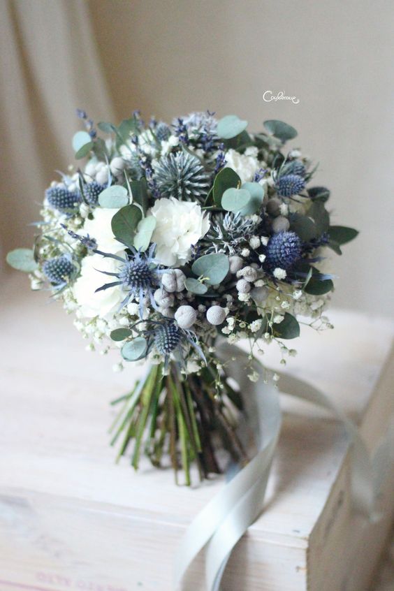 a chic and lovely wedding bouquet of white blooms, baby's breath, blue thistles, greenery and baby's breath is a lovely idea if you love neutrals