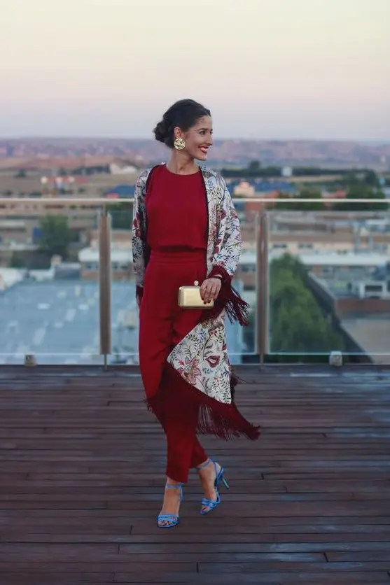 a deep red fitting jumpsuit, a floral fringe kimono, blue shoes, a metallic clutch and matching earrings for the fall