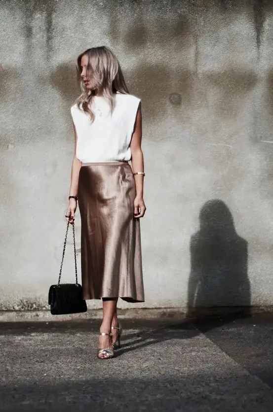a white top with statement shoulders, an elegant taupe midi slip skirt, silver shoes and a black bag