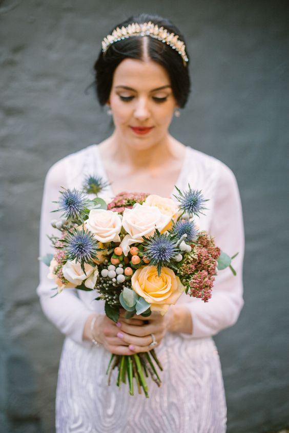 a delicate and catchy wedding bouquet of peachy and blush roses, thistles, berries and greenery is a stunning idea for summer