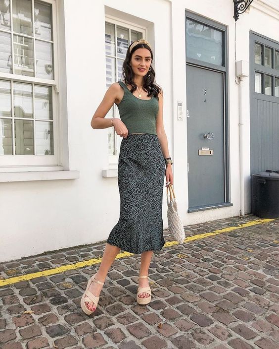 a casual summer wedding guest look with a green crop top, a printed midi skirt, neutral shoes and a woven bag
