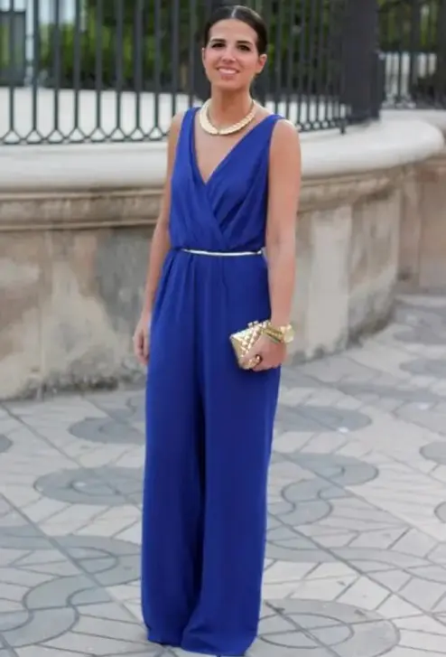 an electric blue jumpsuit with a V-neckline and palazzo pants, with a polished belt, a neckline and a mini clutch for a formal wedding guest look