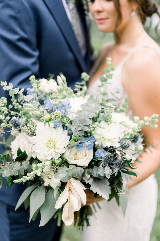 a fantastic wedding bouquet of white roses and dahlias, blue blooms and thistles, foliage and greenery is a lovely idea