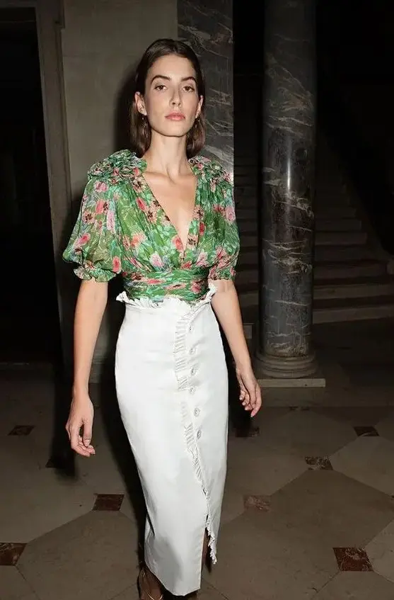 a beautiful wedding guest look with a green floral blouse with a deep V-neckline and a white ruffle skirt with a row of buttons