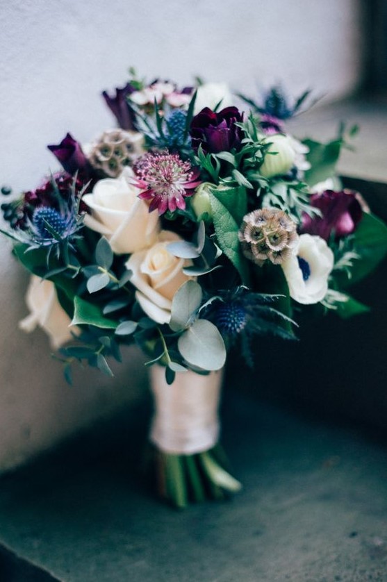 a lovely winter wedding bouquet with white roses, purple ones, anemones, thistles and greenery plus seed pods