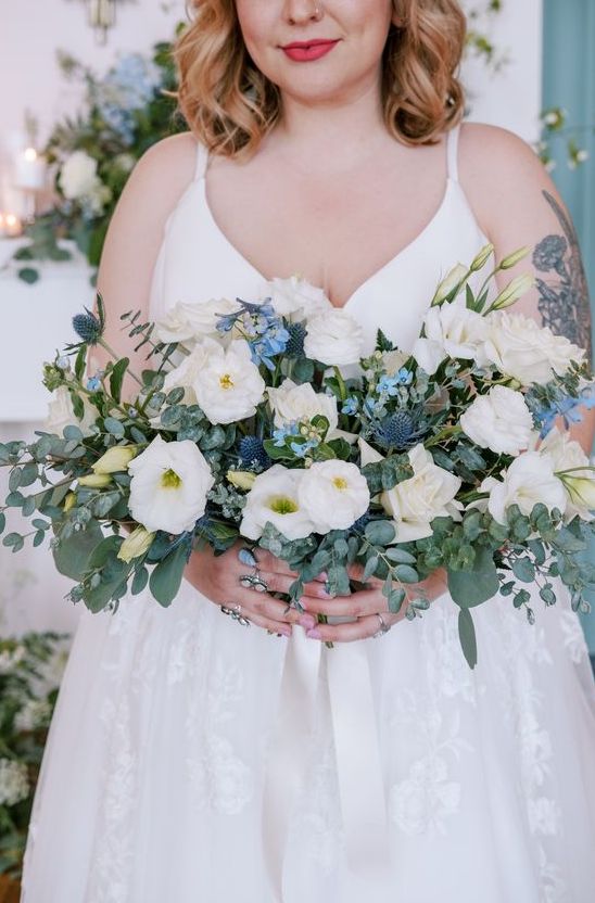 a lush and textured wedding bouquet of white blooms, blue fillers, blue thistles, greenery is a cool idea for a spring or summer wedding