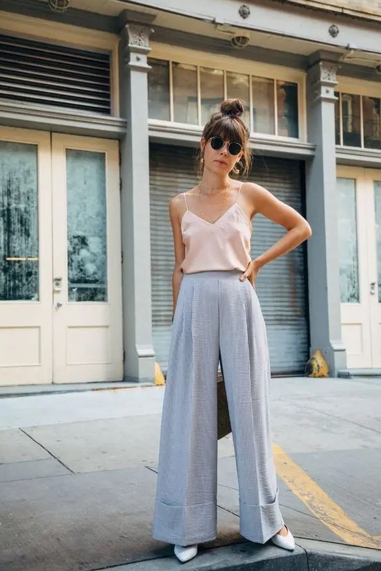 A summer wedding outfit with lavender colored wideleg pants, a blush spaghetti strap top, white shoes and statement earrings