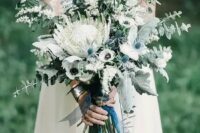 48 a pale and delicate wedding bouquet with blue thistles, a king protea, white anemones and herbs and eucalyptus