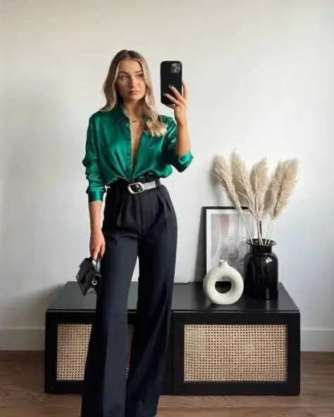 An elegant wedding guest look with an emerald shirt, black high waisted pants, a two tone belt, a tiny black bag