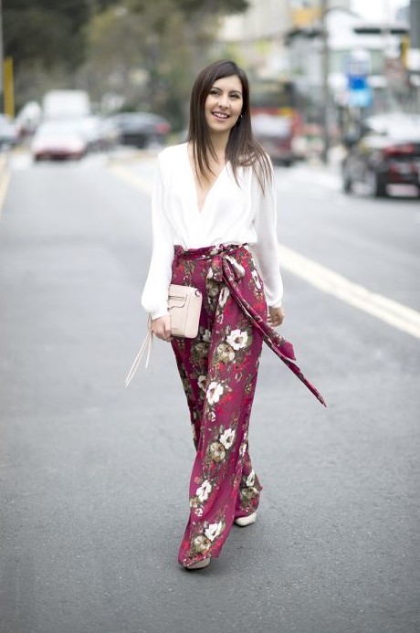 purple floral wideleg pants, a white blouse, a white bag and white heels are great for a summer wedding guest look