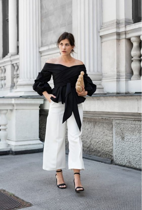 white culottes, a black off the shoulder draped top with long sleeves and ties, black heels and a creative bag