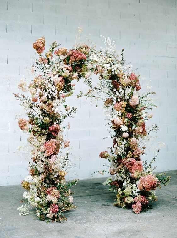 a beautiful and delicate wedding arch done with white and coral hydrangeas, greenery and some blooming branches