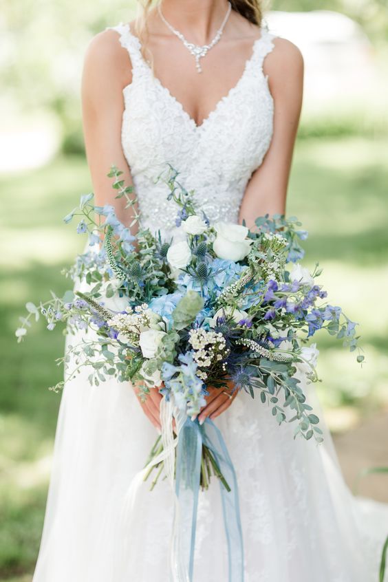 a beautiful and dimensional wedding bouquet with white and blue blooms, thistles, eucalyptus and some purple touches