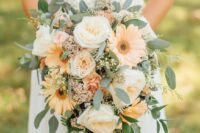 a beautiful and subtle-colored cascading wedding bouquet of white roses, pale orange gerberas and roses, greenery and fillers