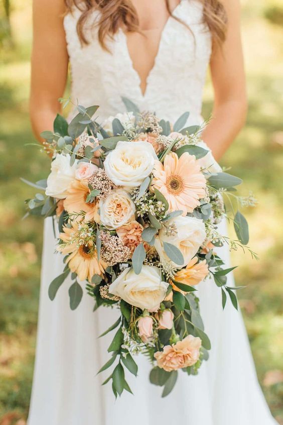 a beautiful and subtle-colored cascading wedding bouquet of white roses, pale orange gerberas and roses, greenery and fillers