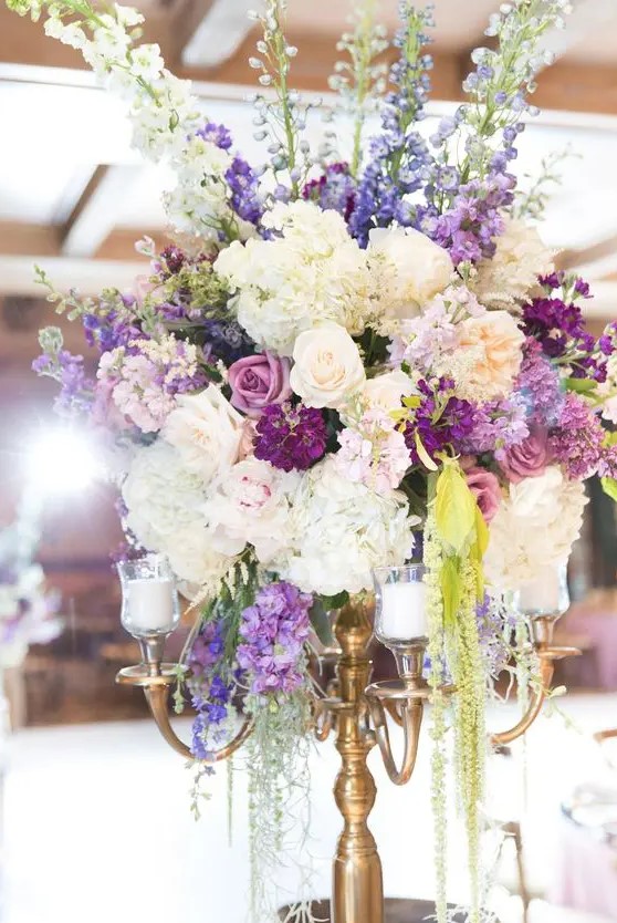 a beautiful and unusual secret garden wedding centerpiece of candles, white, purple and lilac blooms and greenery