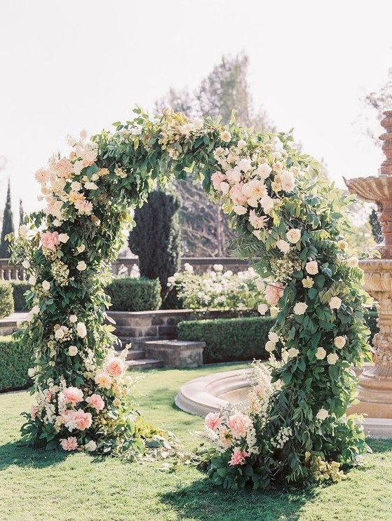 a beautiful circle wedding arch completely covered with greenery and with blush blooms