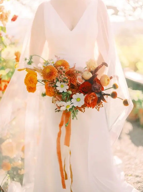 a beautiful fall wedding bouquet with orange dahlias, deep red and burgundy blooms, some blooming twigs and orange ribbon