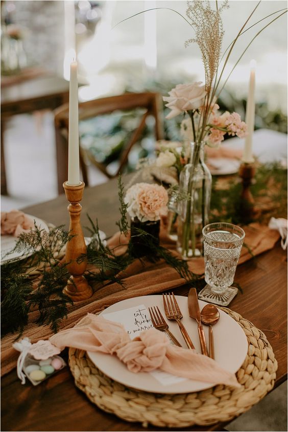 a boho cluster wedding centerpiece of bottles with white roses and blush carnations, some greenery and candles is a cool idea