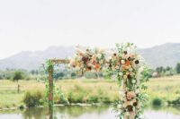 a boho wedding arch done with greenery, white, orange, pink and burgundy dahlias and some pampas grass plus a river view