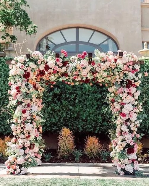 a bold and lush floral wedding arch with white, blush, light pink and burgundy blooms and greenery is amazing