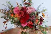 a bold autumnal wedding bouquet of pink and burgundy dahlias, orange and pink roses, seed pods, greenery and ribbons