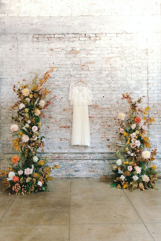 a bold fall wedding altar done with greenery, bright fall leaves, blush, white, mustard and orange dahlias is amazing
