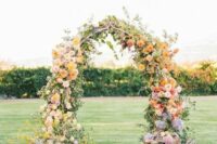 a bold fall wedding arch with blush and mauve roses, yellow dahlias, mauve and blue flowers and greenery is a cool and chic idea