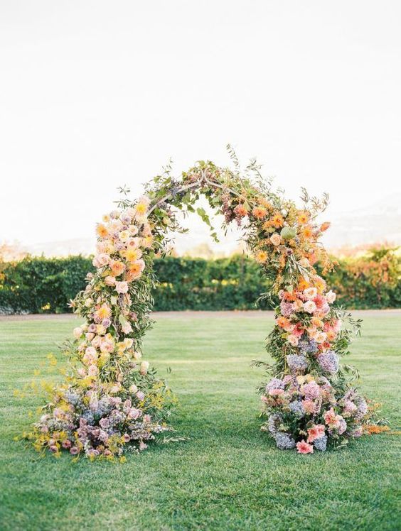 a bold fall wedding arch with blush and mauve roses, yellow dahlias, mauve and blue flowers and greenery is a cool and chic idea