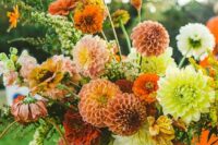 a bold fall wedding arrangement of coral, mauve and white dahlias, sunflowers, lilies, greenery and a tall vase is chic